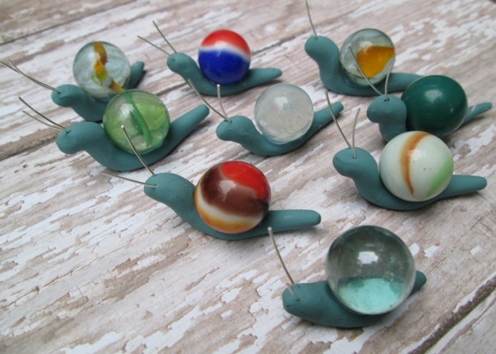 A group of sculpted snails move about on wood, each one has a marble in place of a shell